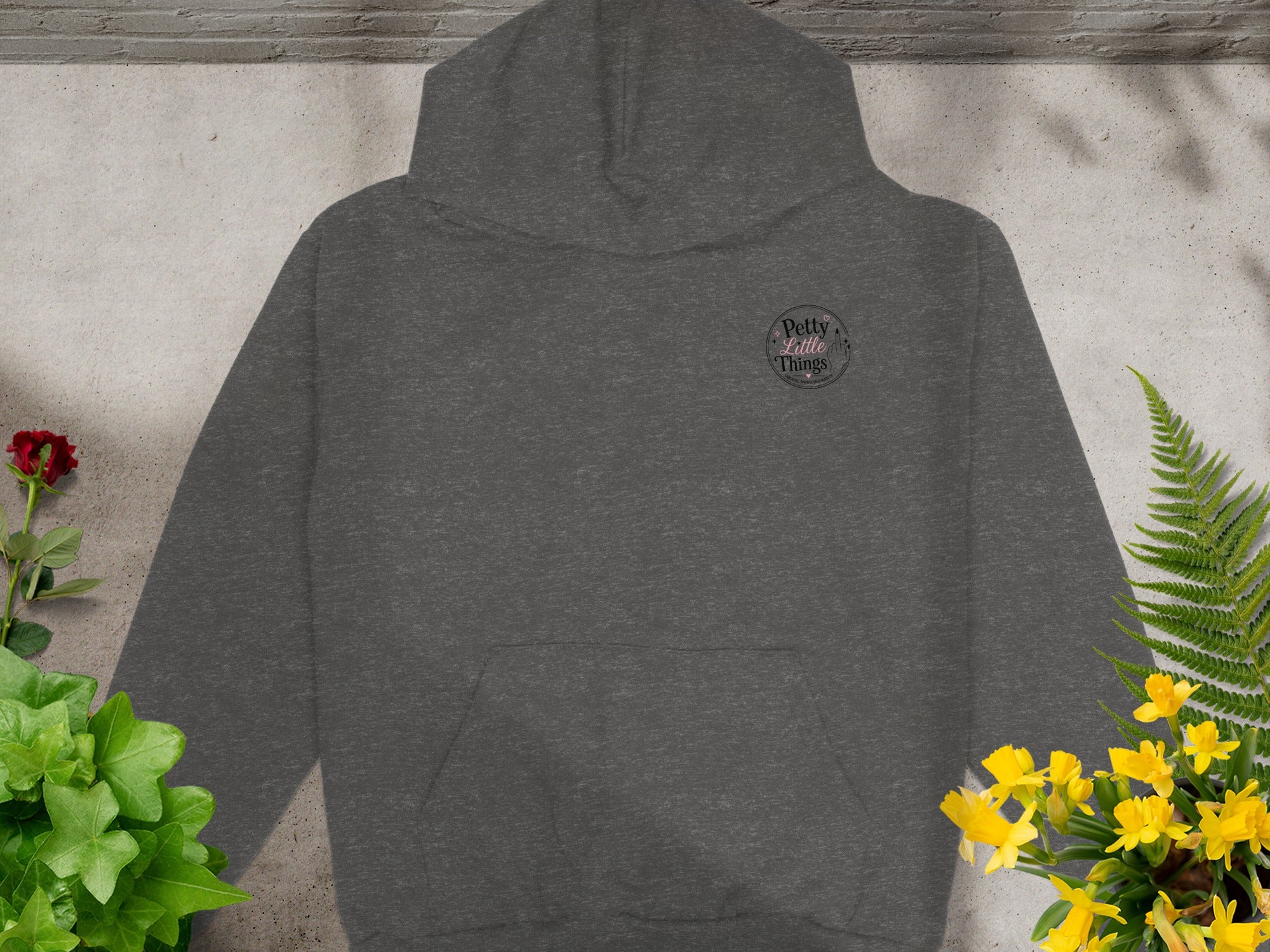 Dark grey hoodie with "Petty Little Things" logo and floral accents.