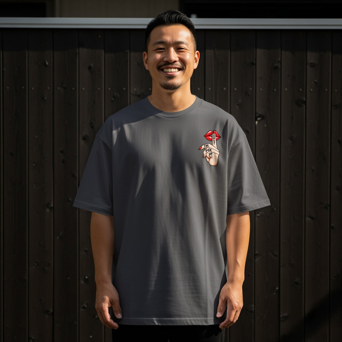 Man in charcoal t-shirt with "Shut The Fuck Up" graphic on left chest.