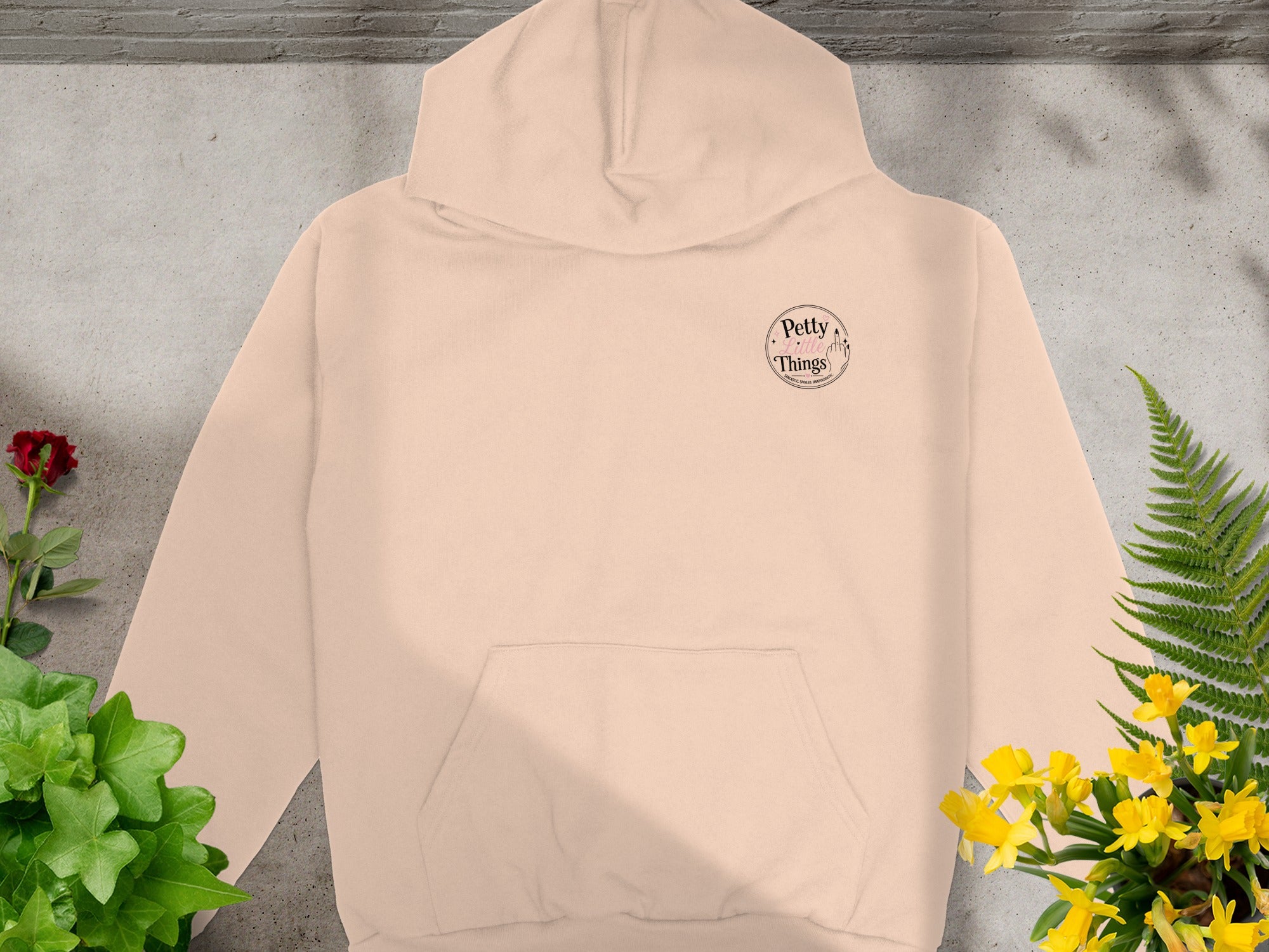 Peach hoodie with a round "Petty Little Things" logo and surrounding text.