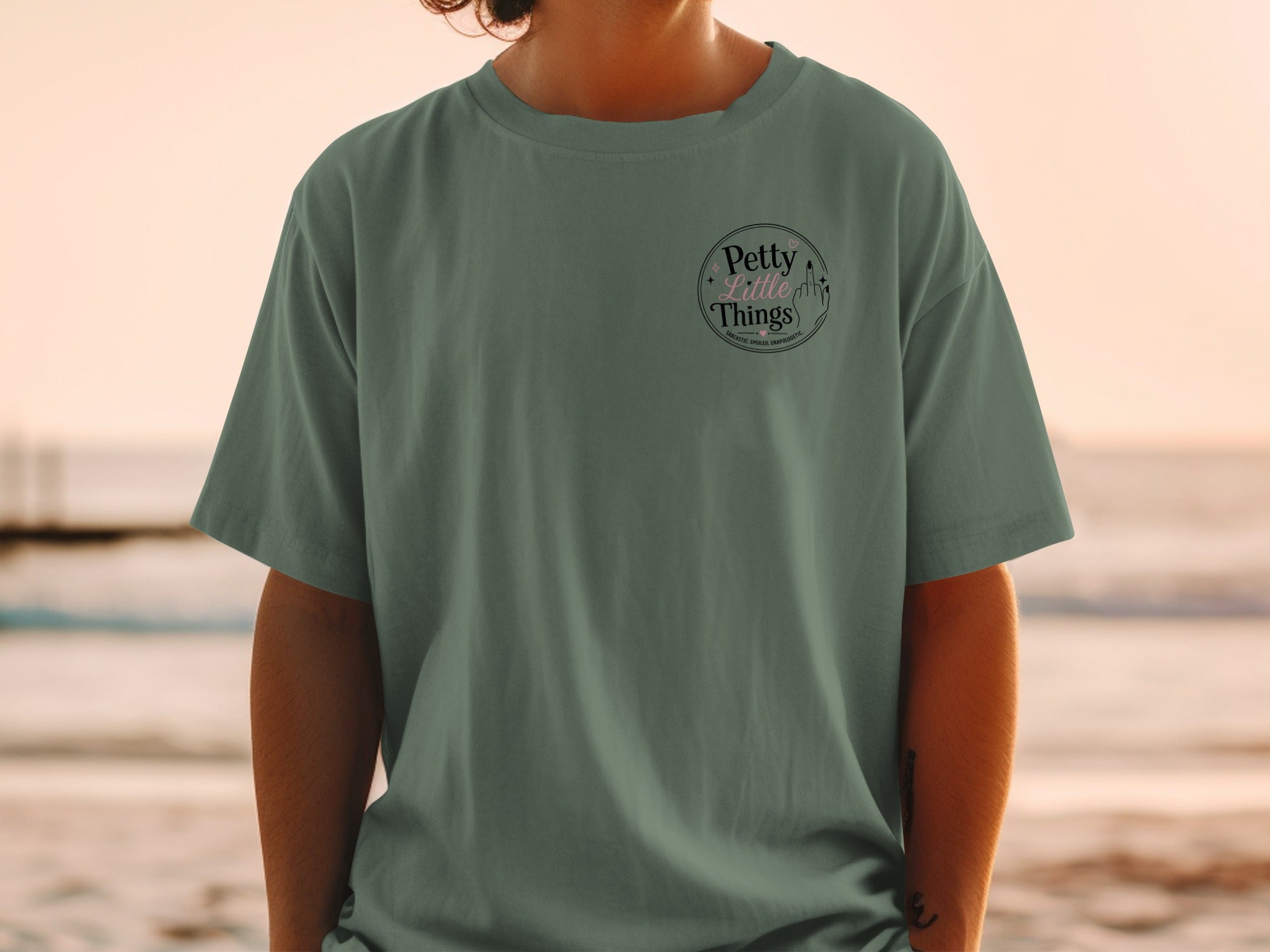 Green t-shirt with a circular graphic containing text "Petty Little Things" and a middle finger.