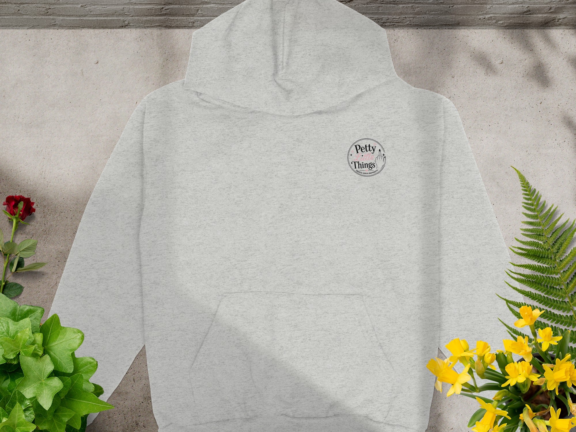 Light grey hoodie with "Petty Little Things" logo on chest, surrounded by plants.